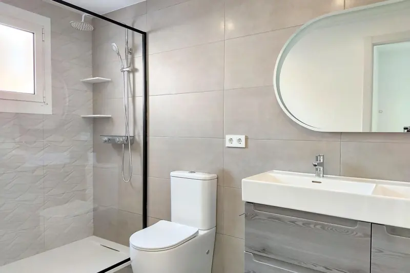 Baño gris con espejo ovalado y mampara negra