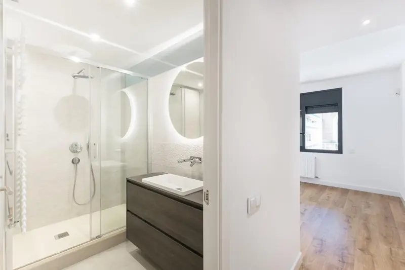 Baño con espejo retroiluminado y mueble oscuro