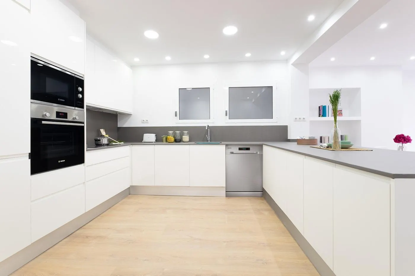 Cocina blanca en L con columnas de horno y suelo de madera